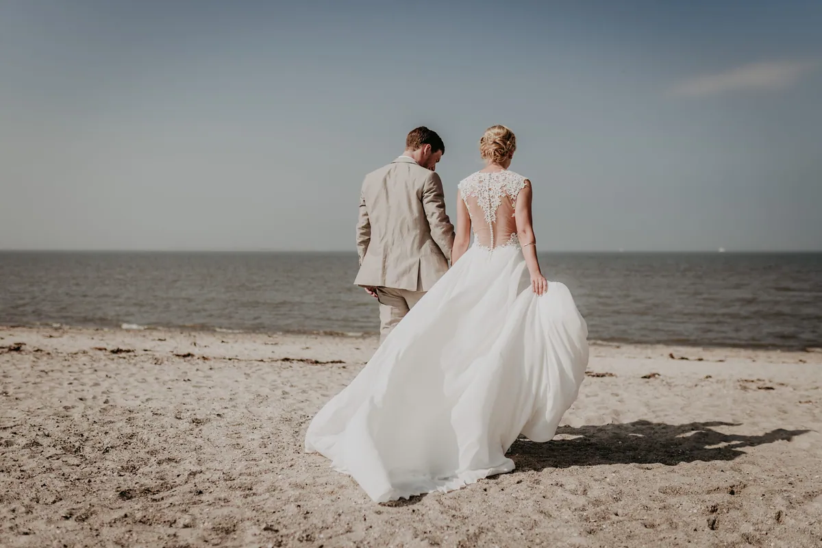 Brautpaar läuft Hand in Hand über den Nordseestrand, das Brautkleid weht im Wind