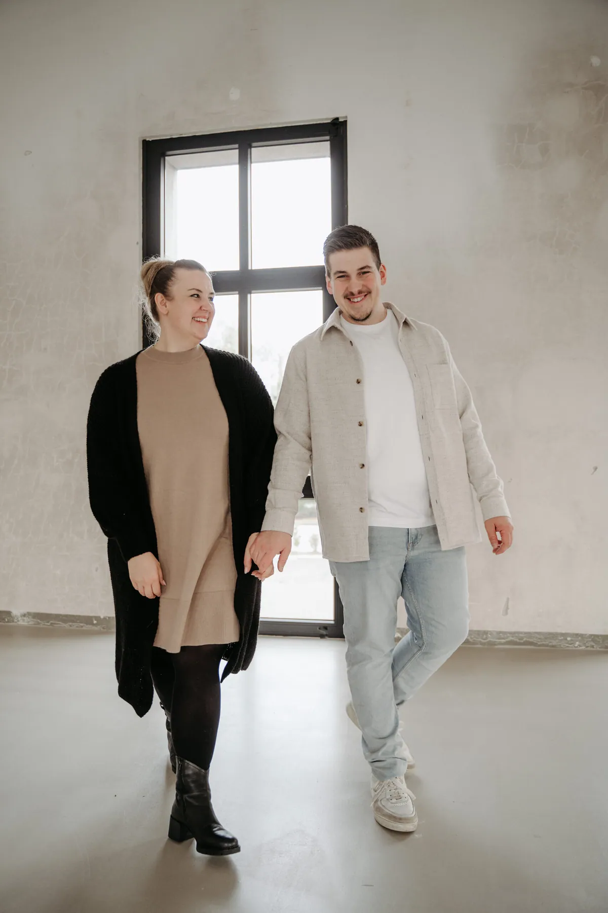 Julia und Jan gehen lachend nebeneinander durch ein helles Studio